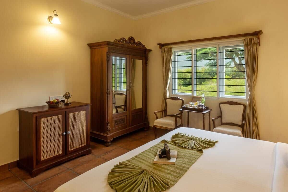 A hotel room with a bed, a wooden wardrobe, a desk, two chairs, and a window with curtains.
