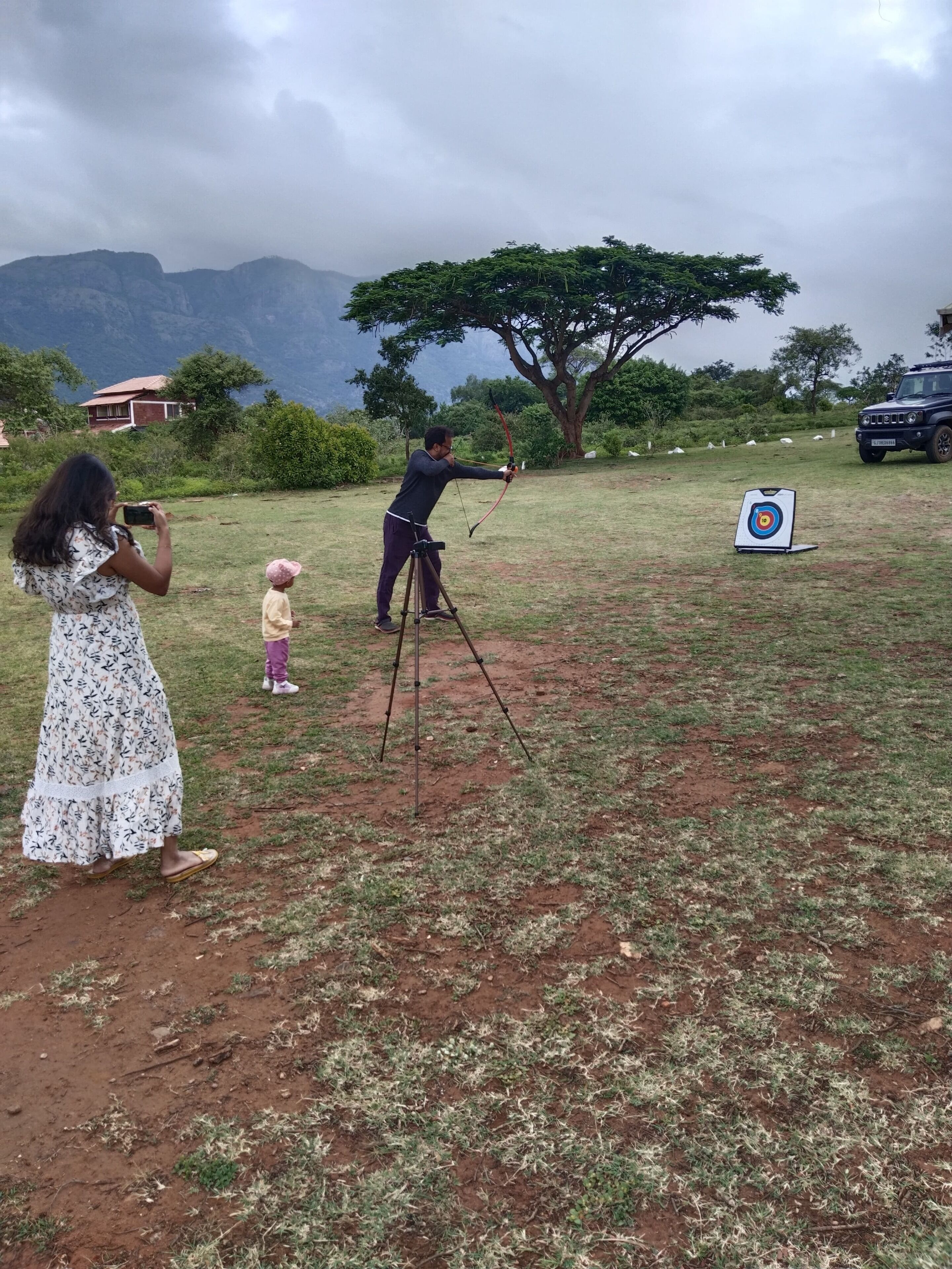 A grassy outdoor area with a target for archery, a tripod, and a vehicle in the background.