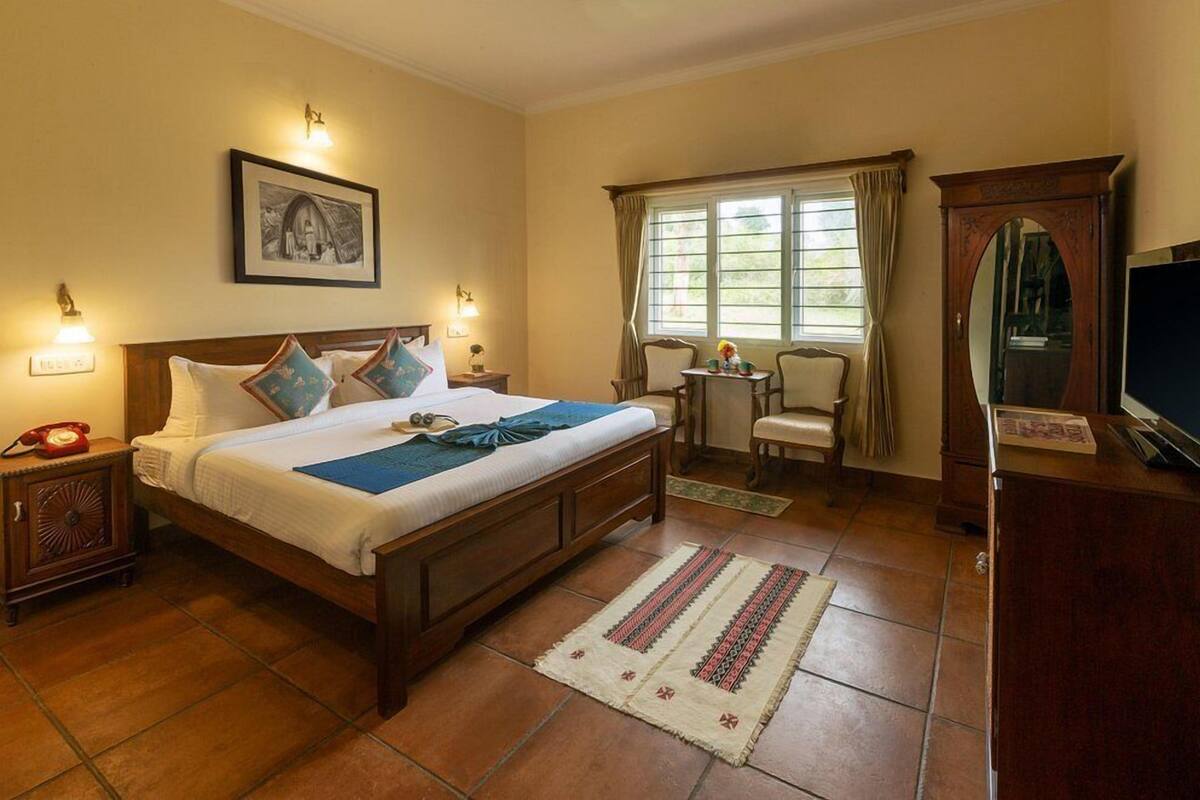 A hotel room with a large bed, a small table with chairs, a television, and a framed picture on the wall.