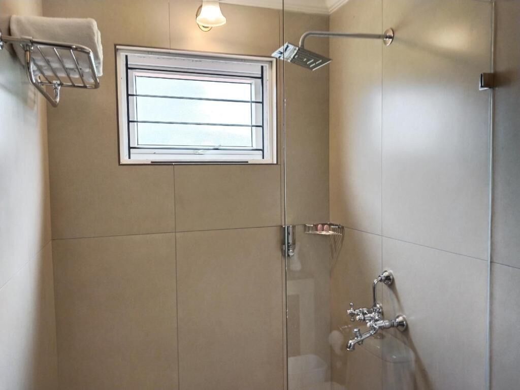 A modern bathroom with a glass shower enclosure, a window, and a towel rack.