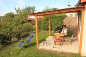 A covered patio with a table and chairs, surrounded by greenery and a wooden fence. - Holiday Homes for 3 People in Lubin (Międzyzdroje)