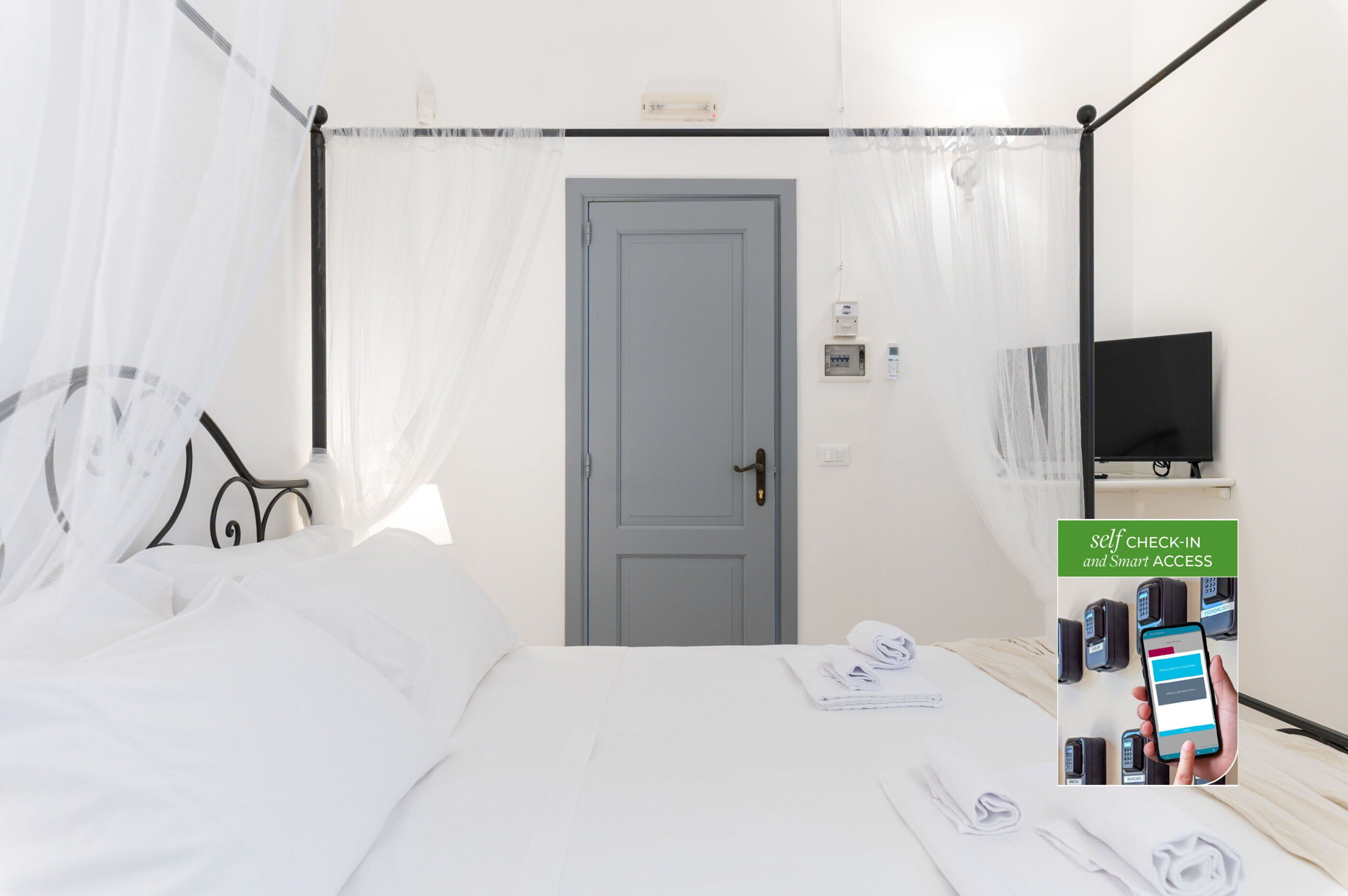 Habitación de hotel con cama, televisor montado en la pared, puerta y quiosco de auto-registro.