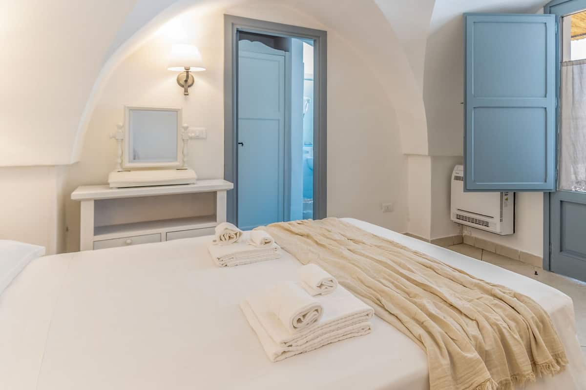 Ein Schlafzimmer mit einem Bett, einem Schminktisch mit Spiegel und einer Tür zu einem anderen Raum.