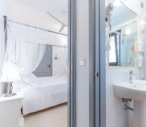 A modern bedroom with a canopy bed, a bedside table with a lamp, and a bathroom with a sink and mirror. - Masseria Lamagrotte By Raro Rooms (Ostuni)