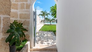 An arched doorway leading to a pool area with a clear blue sky and palm trees. - Masseria Lamagrotte By Raro Rooms (Ostuni)