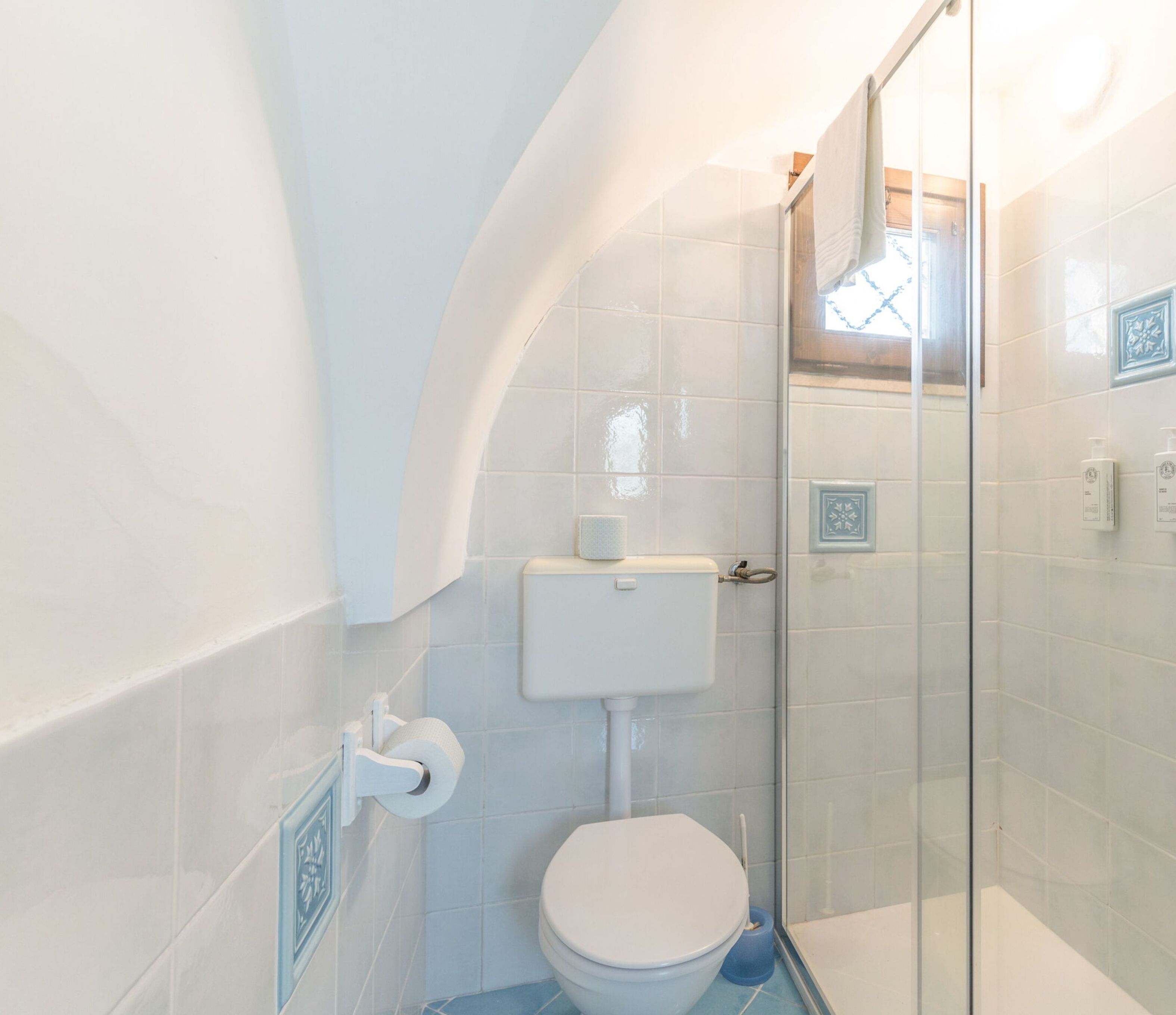 Et badeværelse med toilet, glas brusekabine og toiletpapirholder.
