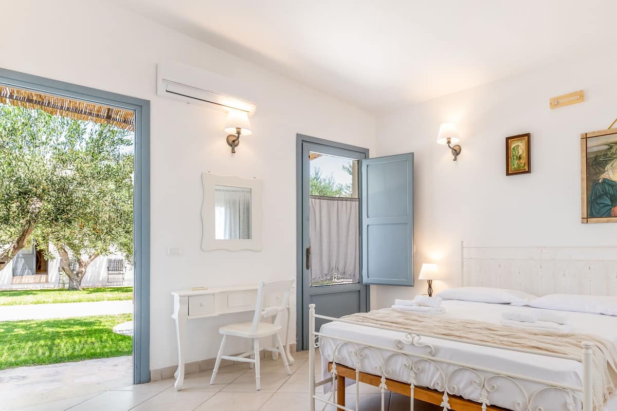 Ein Schlafzimmer mit Bett, Schreibtisch und Stuhl. Ein Fenster bietet Blick auf Grünfläche.
