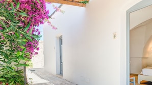 A narrow stone-paved pathway leading to a white building with a blue door and a bed visible inside. - Masseria Lamagrotte By Raro Rooms (Ostuni)