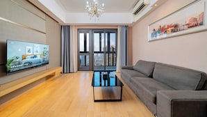 A modern living room with a flat-screen TV, a glass coffee table, a grey sofa, and a large window with curtains. - Heefun International Apartment - Free Shuttle to Canton Fair (Guangzhou)