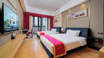 A hotel room with two beds, a TV, a desk, and a view of the city.