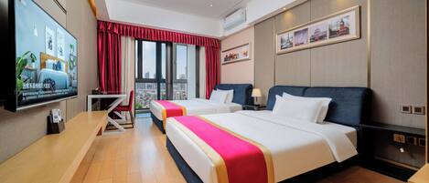 A hotel room with two beds, a TV, a desk, and a view of the city.