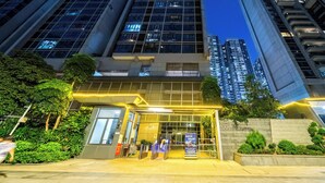 A modern building with a glass facade, a well-lit entrance, and a landscaped area with greenery. - Heefun International Apartment - Free Shuttle to Canton Fair (Guangzhou)