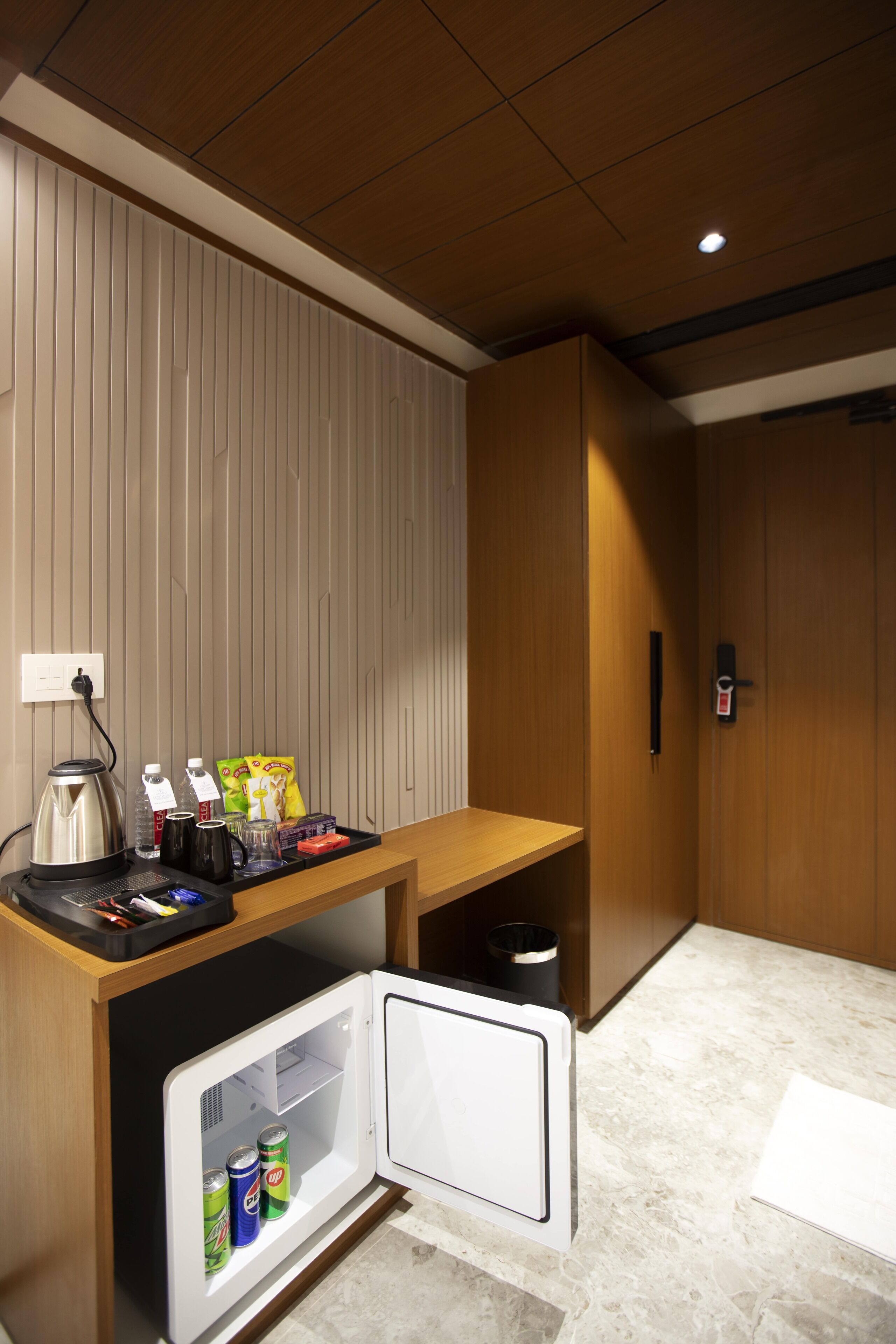 Una kitchenette compacta con refrigerador integrado, cafetera y una pequeña encimera con snacks y hervidor.