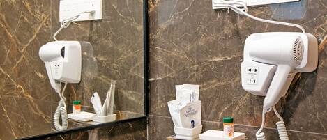 Un baño con pared de mármol, un lavamanos, un espejo y dos secadores de pelo fijos en la pared.