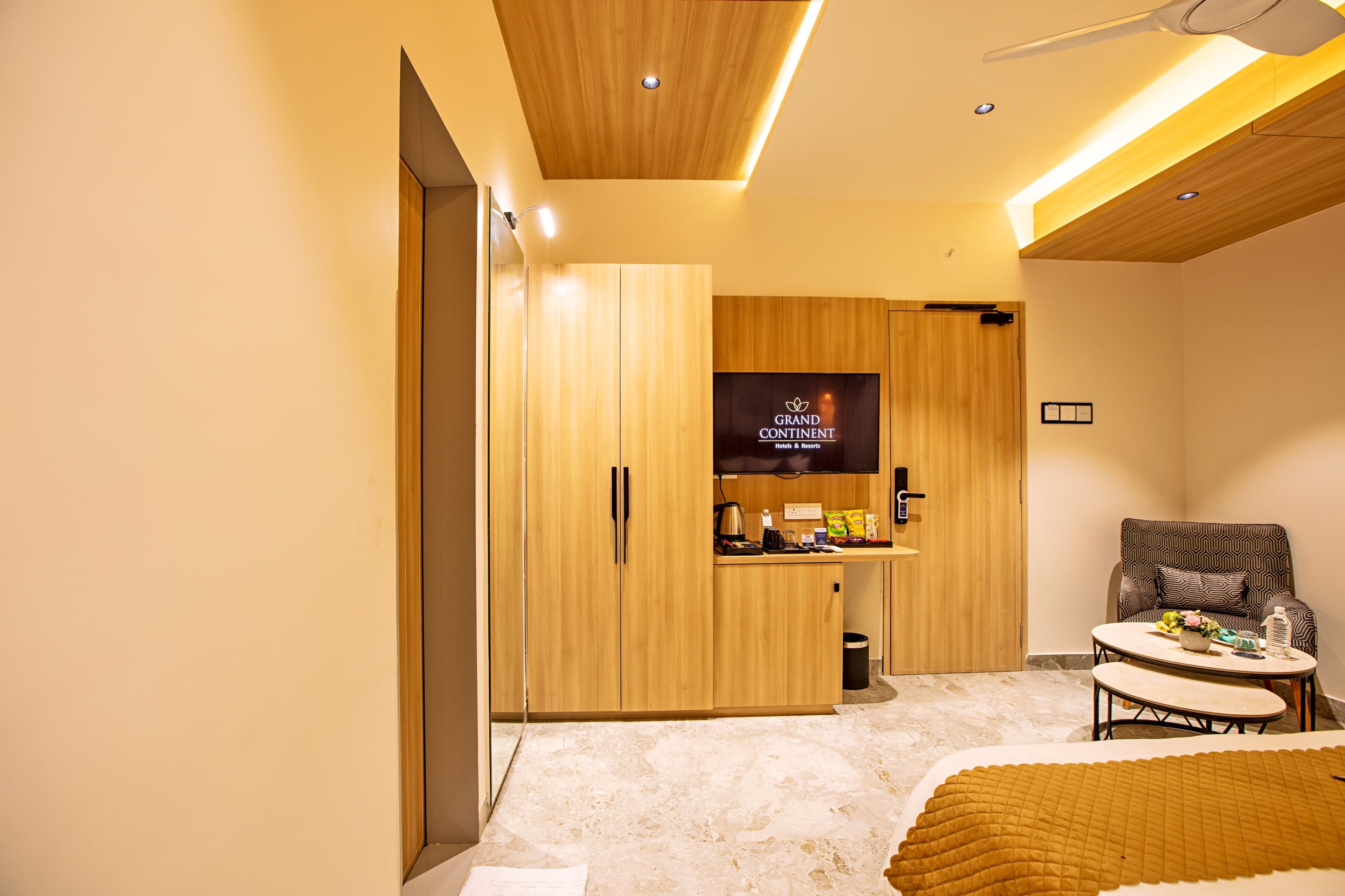 A hotel room with a wooden wardrobe, a television, a sofa, and a small table.