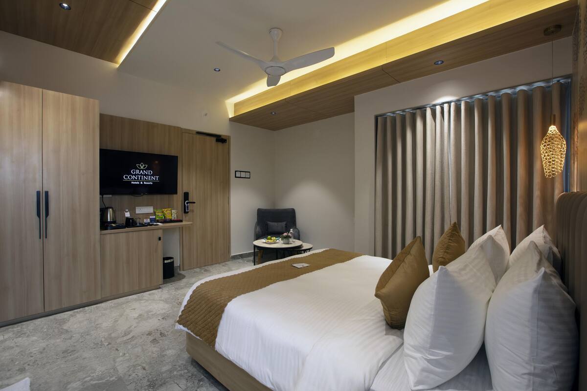 A modern hotel room with a large bed, a flat-screen TV, wooden cabinets, and a ceiling fan.