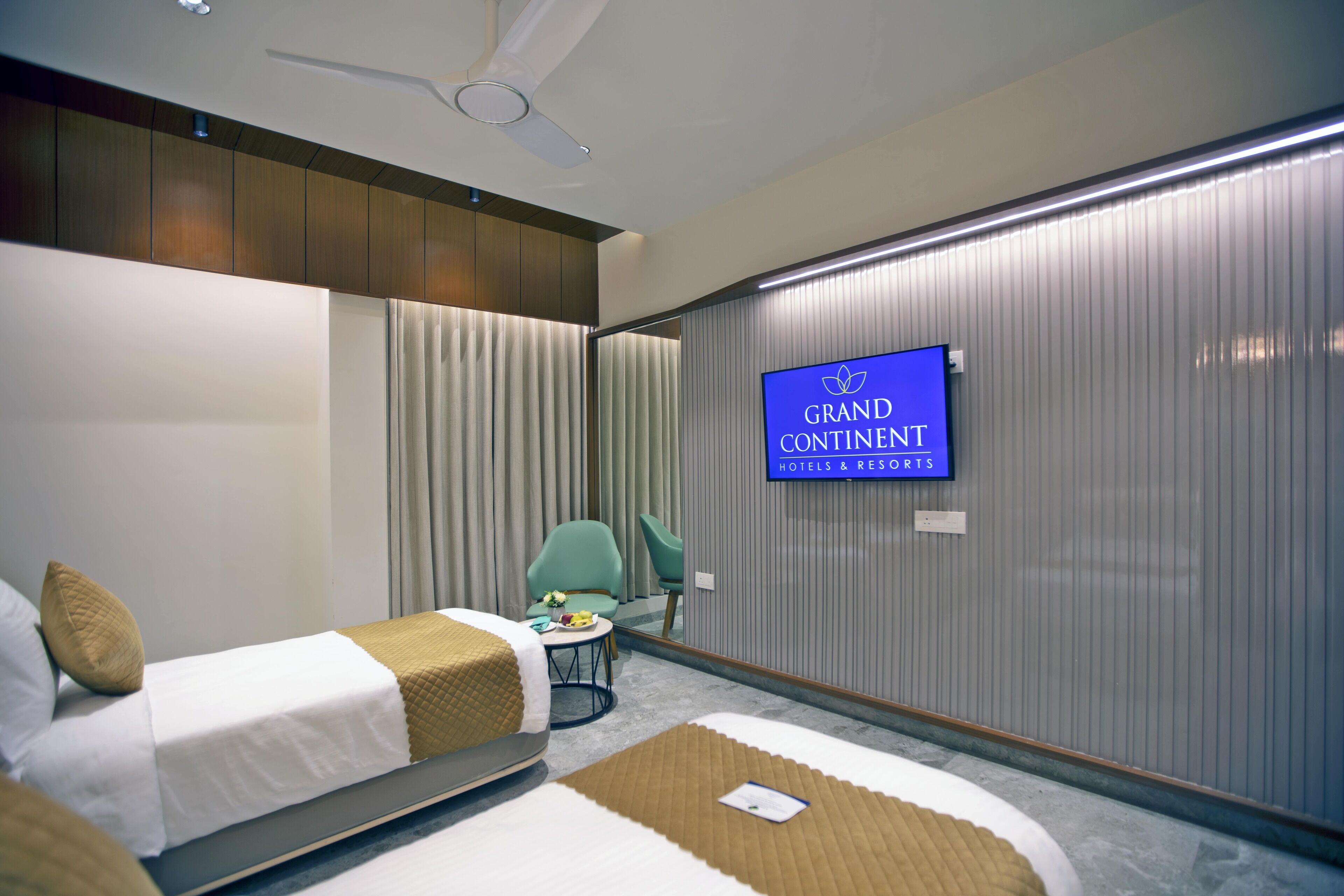 Une chambre d’hôtel avec deux lits, une télévision, un ventilateur de plafond et une vue sur l’enseigne du Grand Continental Hotels & Resorts.