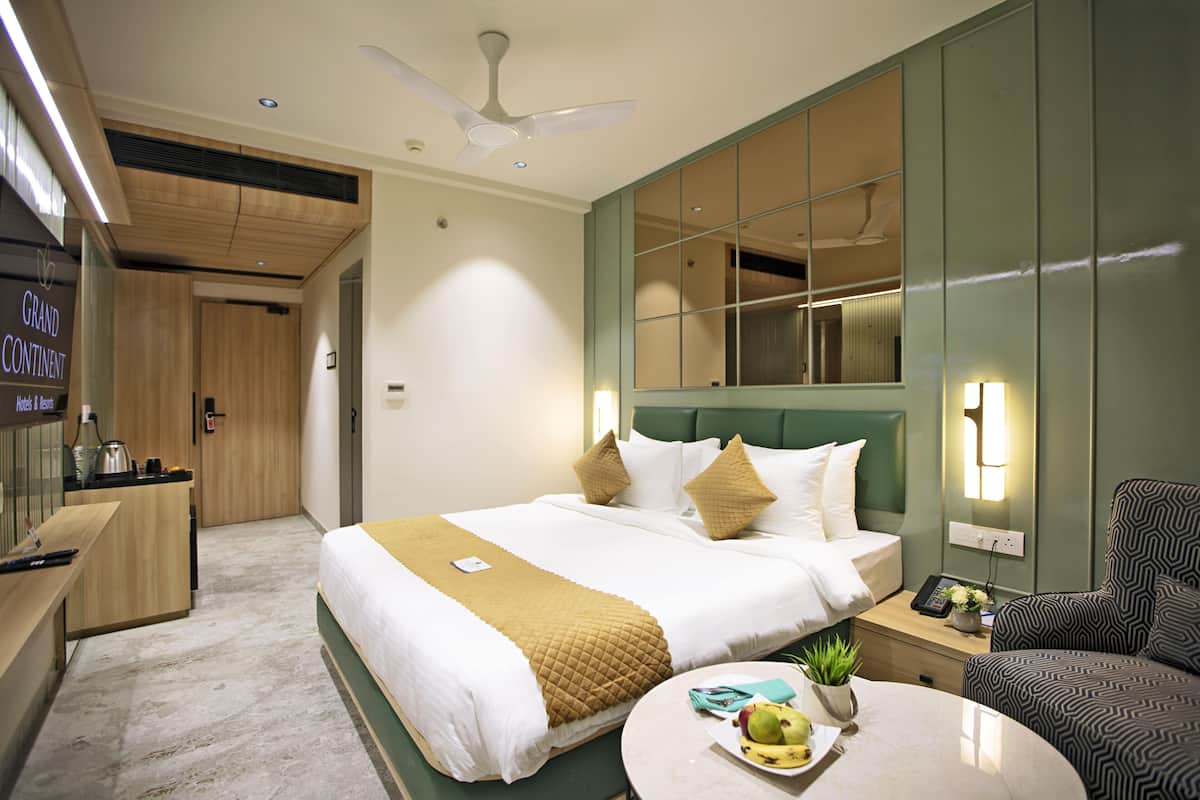 A hotel room with a bed, bedside table, chair, and a small round table with a fruit bowl.