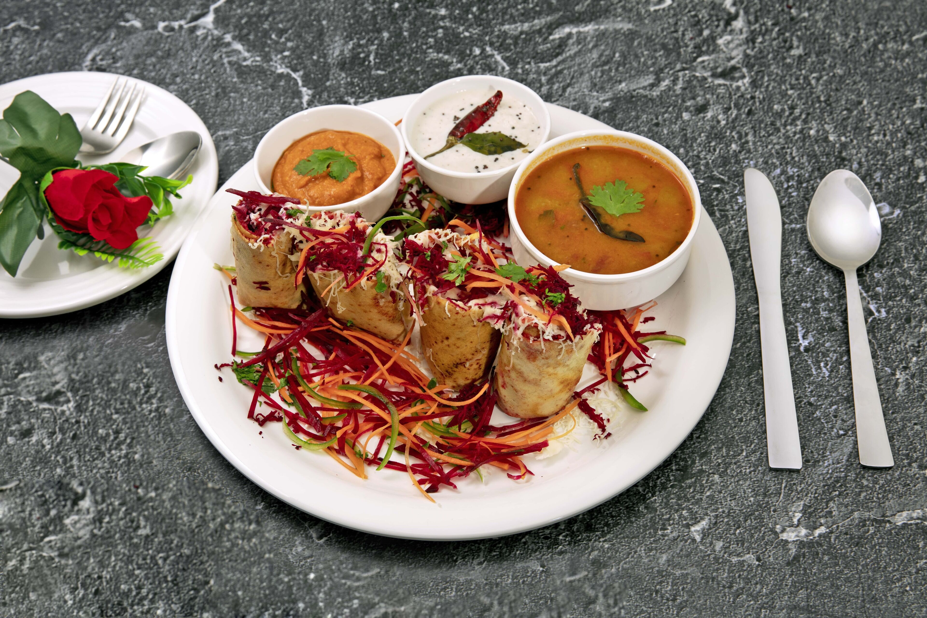 A plate of food with a red rose, a bowl of soup, and a plate of vegetables.