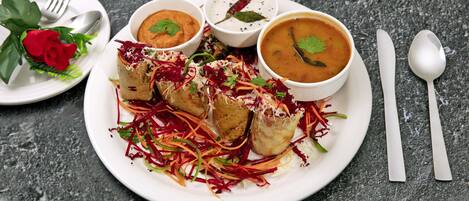 A plate of food with a red rose, a bowl of soup, and a plate of vegetables.