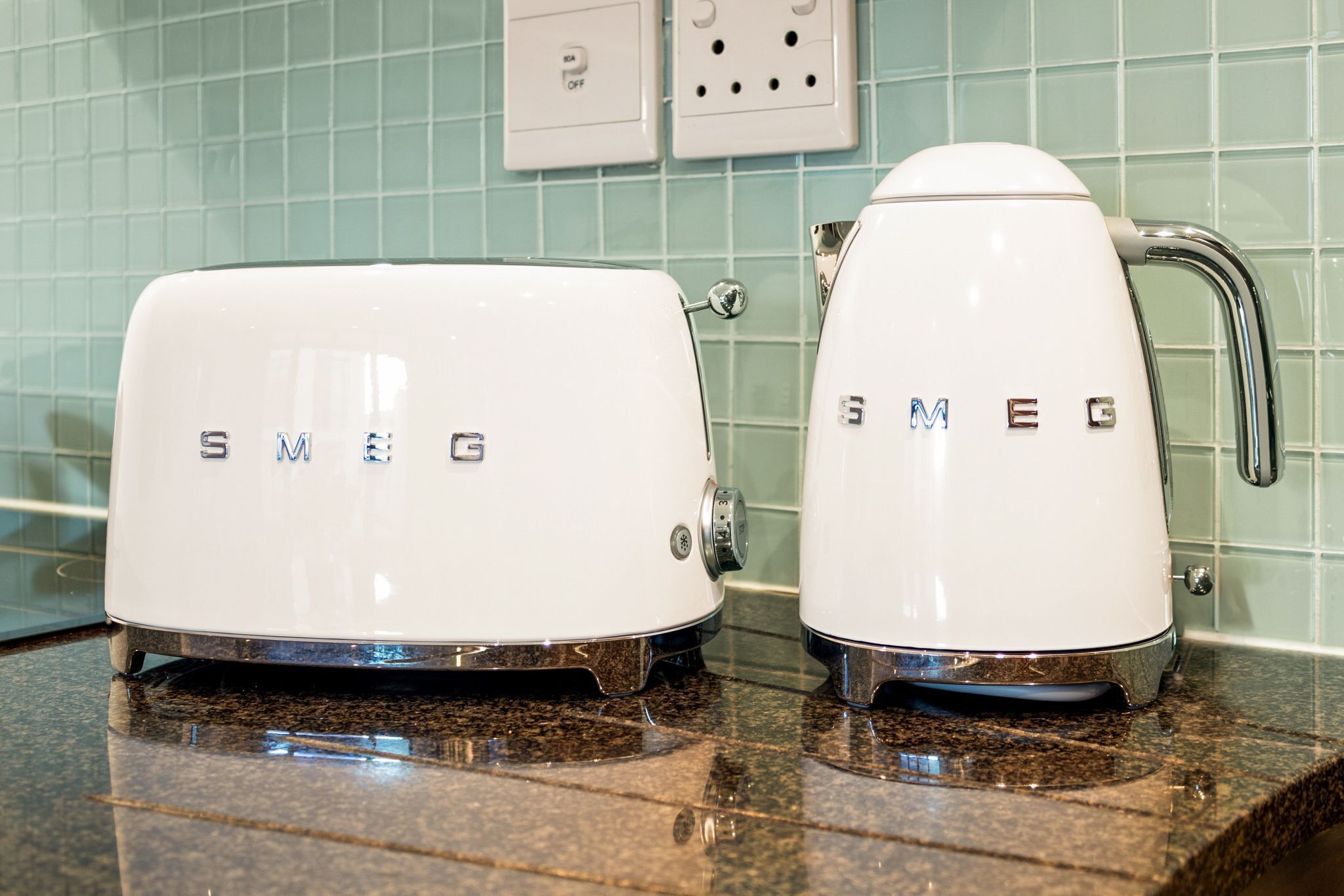 Two white electric kettles with the brand name "SMEG" on a kitchen countertop.