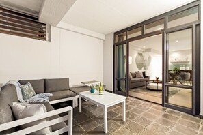 A modern living room with a grey sofa, a white coffee table, and a glass door leading to a dining area.