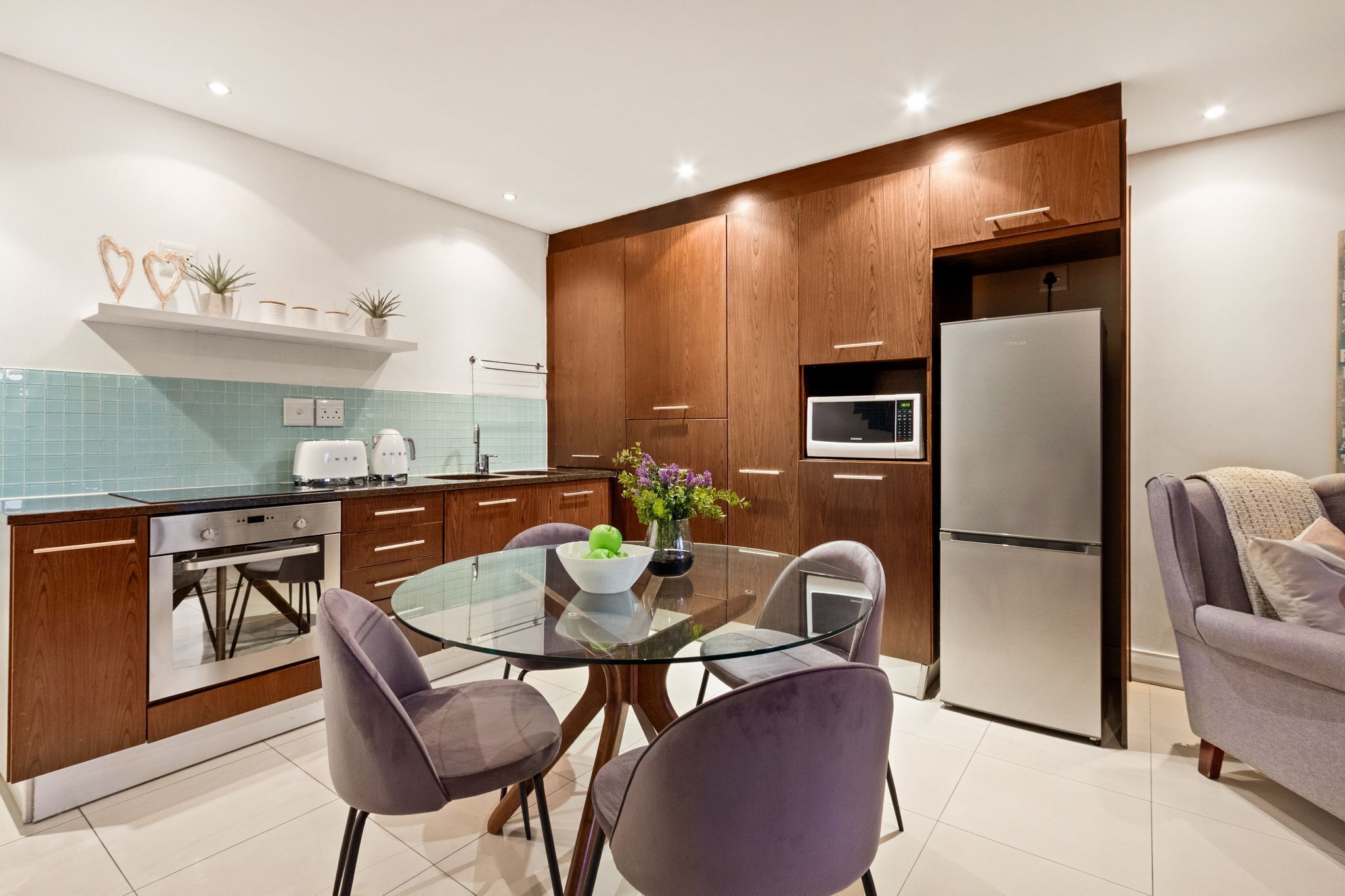 Una cocina moderna con armarios de madera, una mesa de comedor de vidrio y un microondas empotrado.