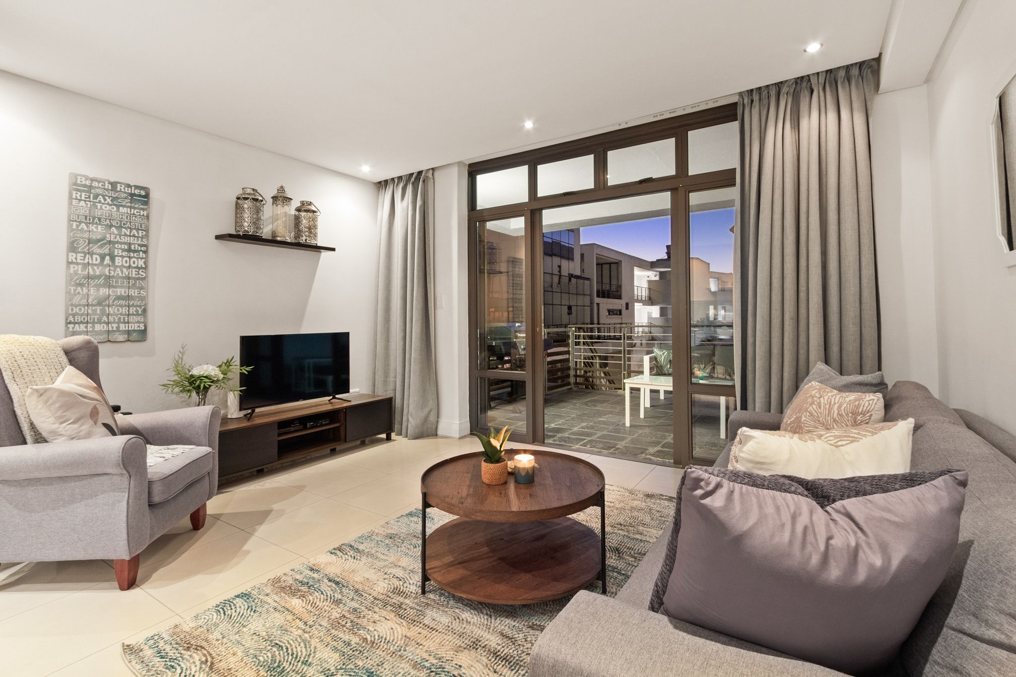 A modern living room with a sofa, armchair, coffee table, TV, and a large window with curtains.