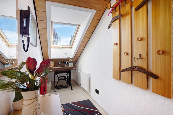 A room with a sloped ceiling, wooden walls, a radiator, a sewing machine, a telephone, and a door with a coat hanger.