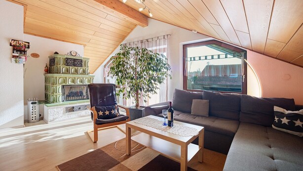 A cozy loft apartment with a wooden ceiling, a green cabinet, a large window, a sofa, a coffee table, and a chair.