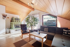 A cozy loft apartment with a wooden ceiling, a green cabinet, a large window, a sofa, a coffee table, and a chair.