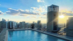 Una piscina en la azotea con sillones de descanso y vista al horizonte urbano.