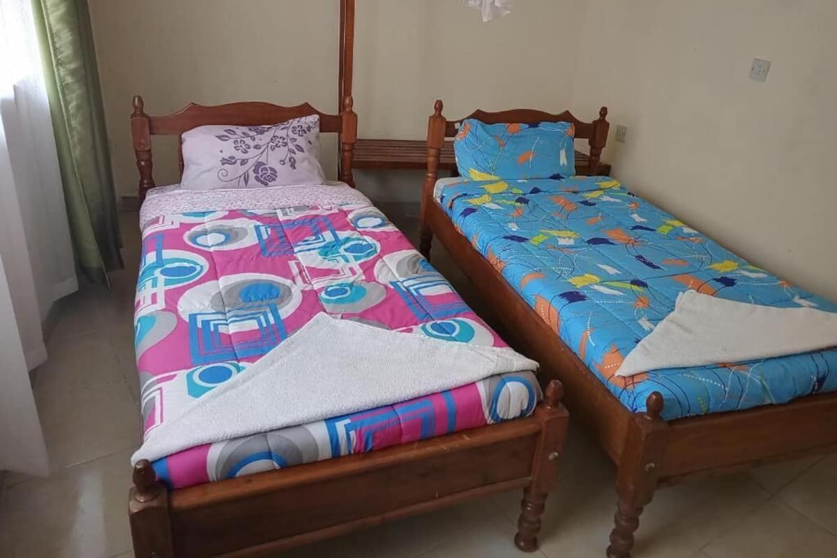 Two wooden beds with colorful bedding, a wooden headboard, and a curtain on the left.
