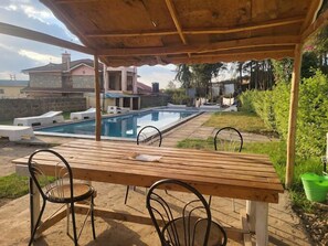 Ein überdachter Außenbereich mit Pool, Holztisch und Stühlen.