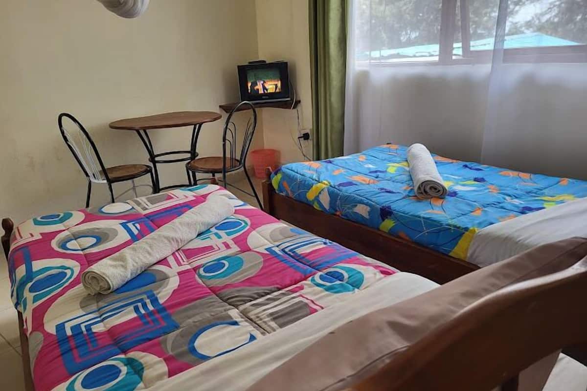 A room with two beds, a small table, a chair, and a television.