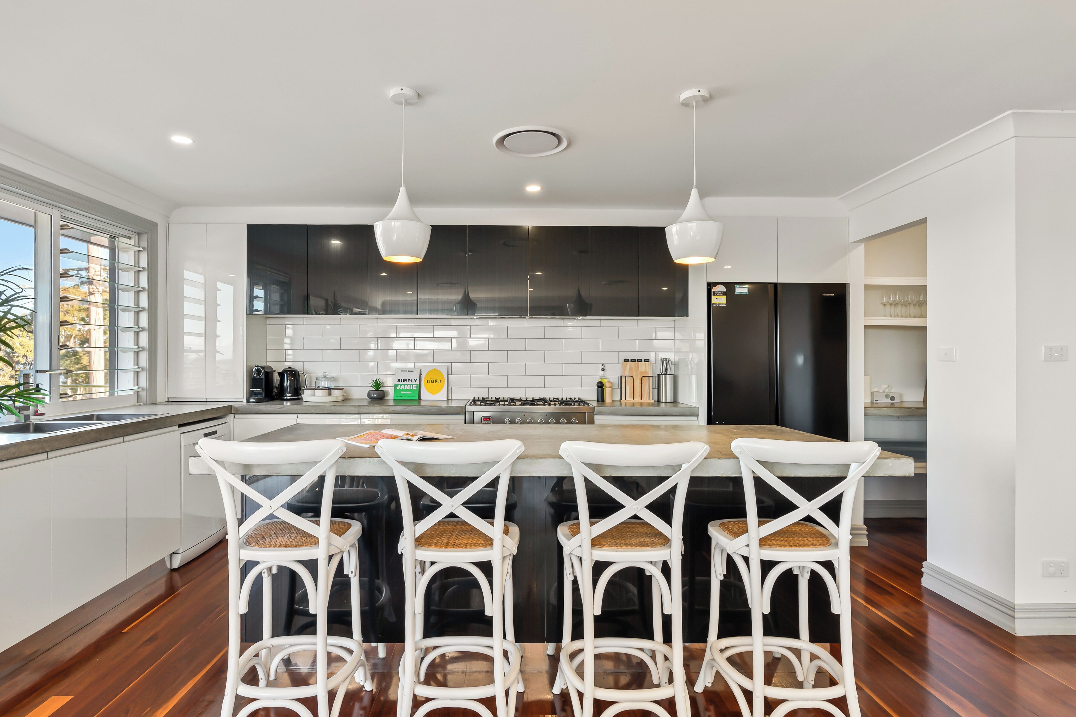 A modern kitchen with white cabinetry, a central island with bar stools, pendant lighting, and a view of the outdoors.