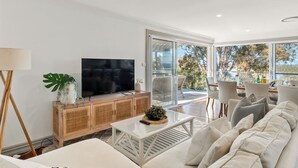 Een moderne woonkamer met een flatscreen televisie, een houten kast, een witte bank en een glazen deur naar een terras.