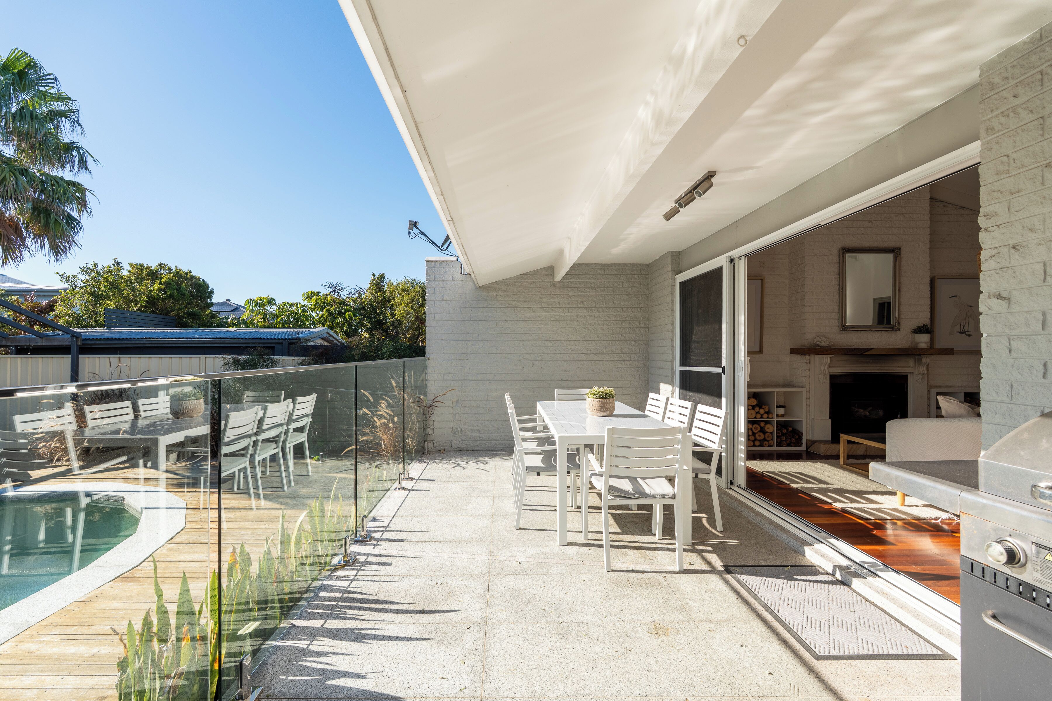 A patio with a pool, white furniture, and a barbecue area.