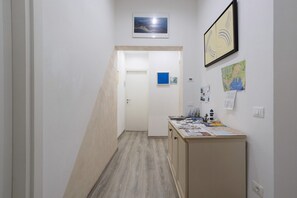 Un couloir avec un plancher en bois, une porte au fond et un bureau avec des papiers et une carte accrochée au mur.
