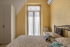 Une chambre à coucher avec un lit, des oreillers, une armoire, un radiateur et une fenêtre avec des rideaux.