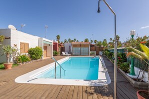 A swimming pool with a wooden deck, surrounded by potted plants and palm trees.