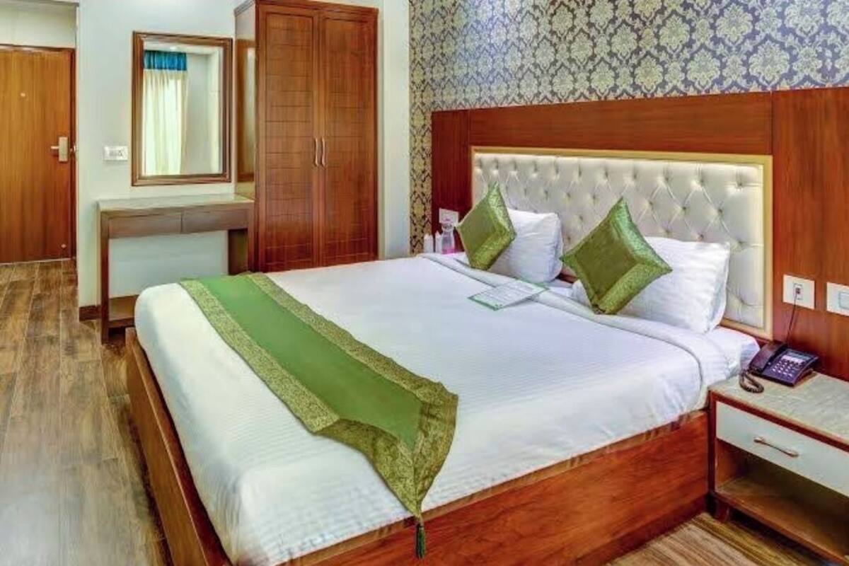 A hotel room with a large bed, wooden wardrobe, and a bedside table with a telephone.
