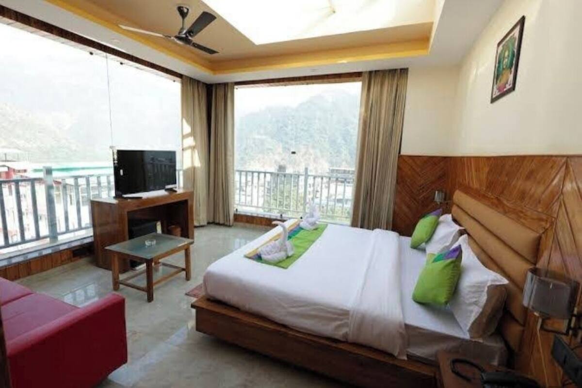 A hotel room with a bed, a TV, a desk, and a balcony with a view of the mountains.