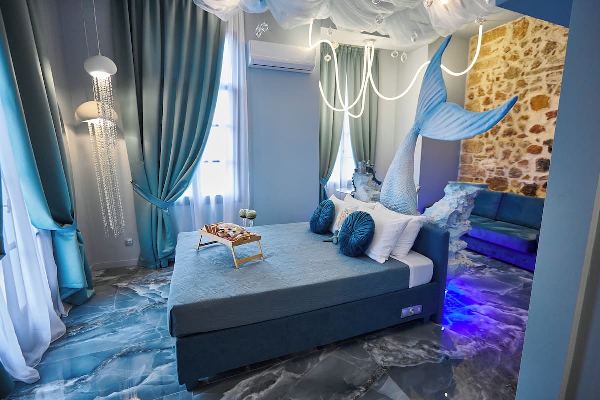 A bedroom with a bed, curtains, a chandelier, and a stone wall.