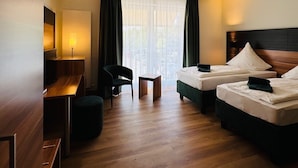 A hotel room with two beds, a desk, a chair, and a small table. - Hotel Sittardsberg (Duisburg)