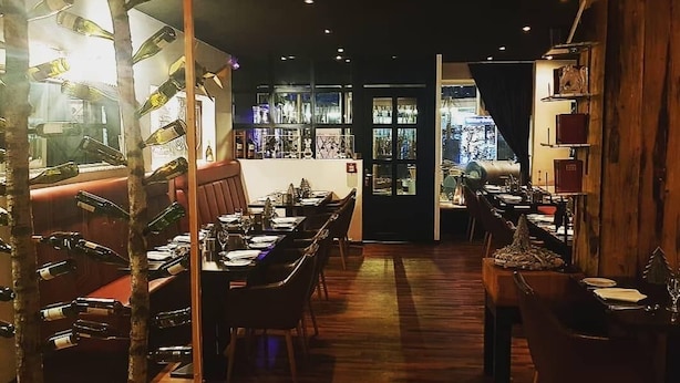 A restaurant with wooden flooring, tables, and chairs. There are bottles hanging on the wall and a bar area visible through a doorway. - Hotel Sittardsberg (Duisburg)