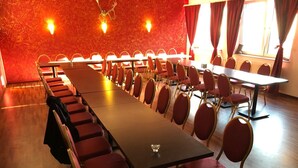 A conference room with long tables and red chairs, a wooden floor, and a red textured wall with ceiling lights. - Hotel Sittardsberg (Duisburg)