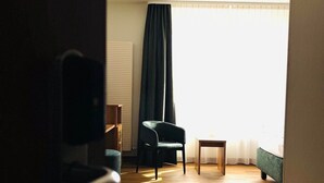A room with a wooden floor, a black chair, a small table, and a bed with a green headboard. - Hotel Sittardsberg (Duisburg)