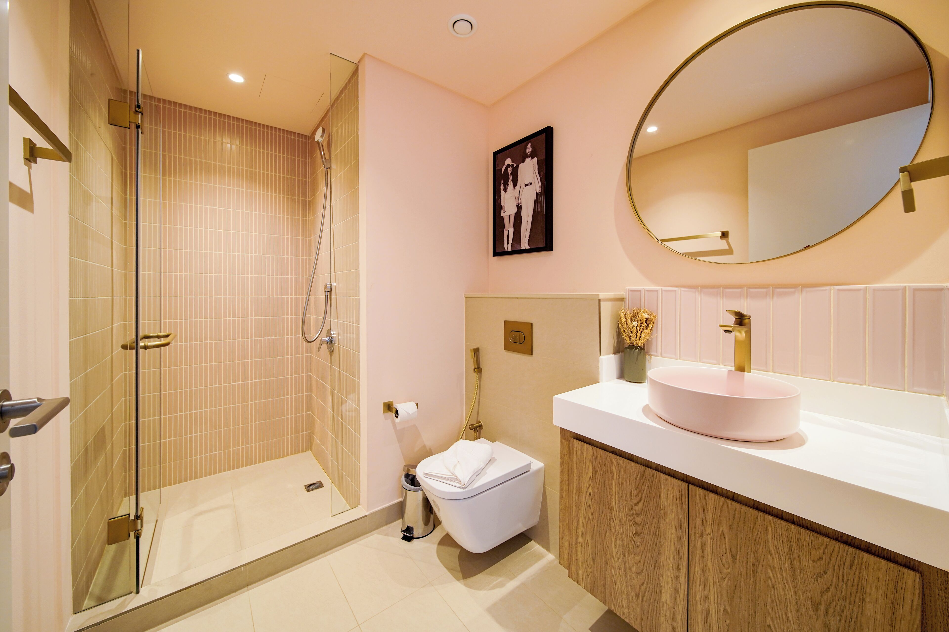Un bagno moderno con doccia vetrata, un water bianco e uno specchio tondo sopra un lavandino rosa.