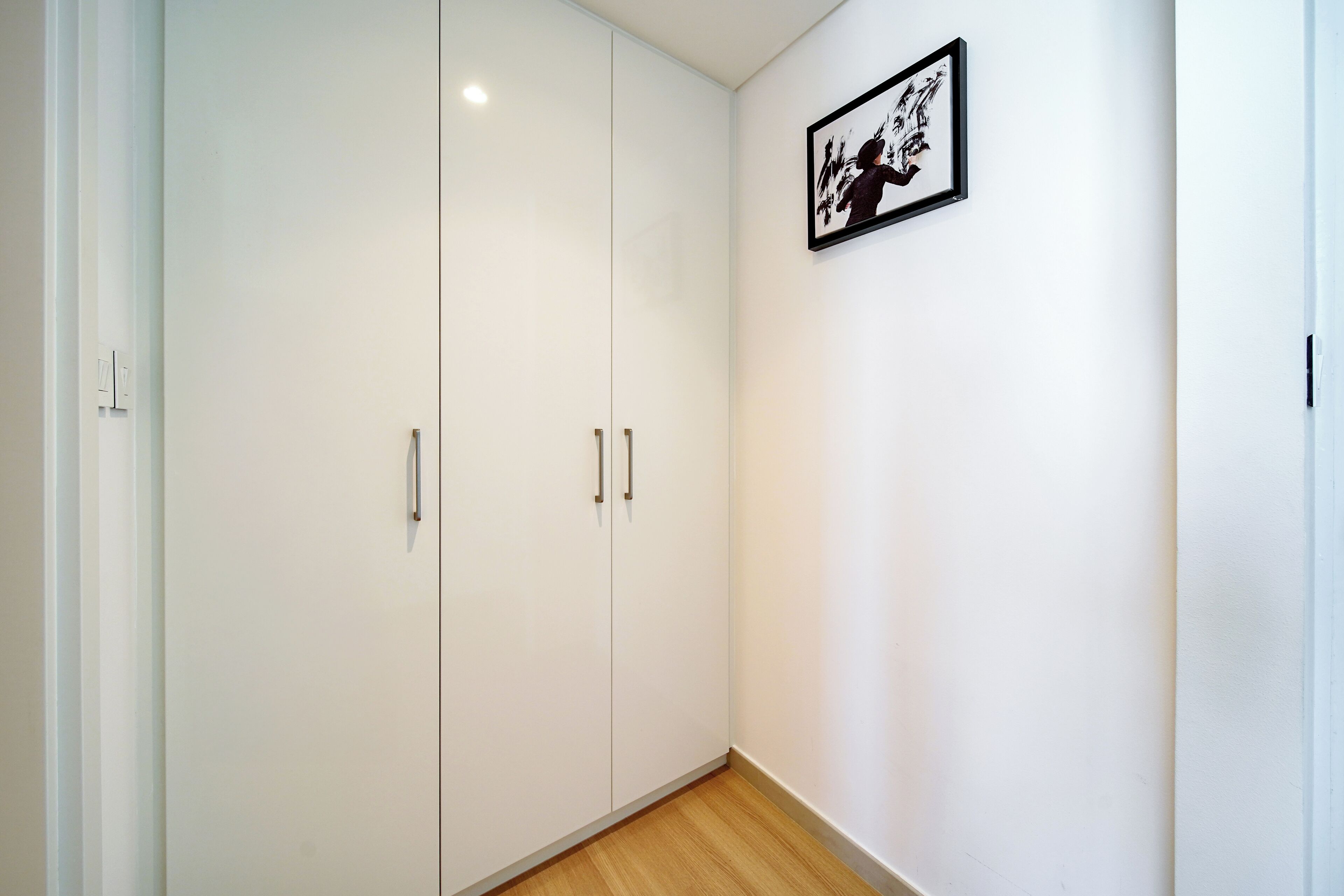 Une pièce avec une armoire blanche, une œuvre d’art encadrée au mur et un plancher en bois.